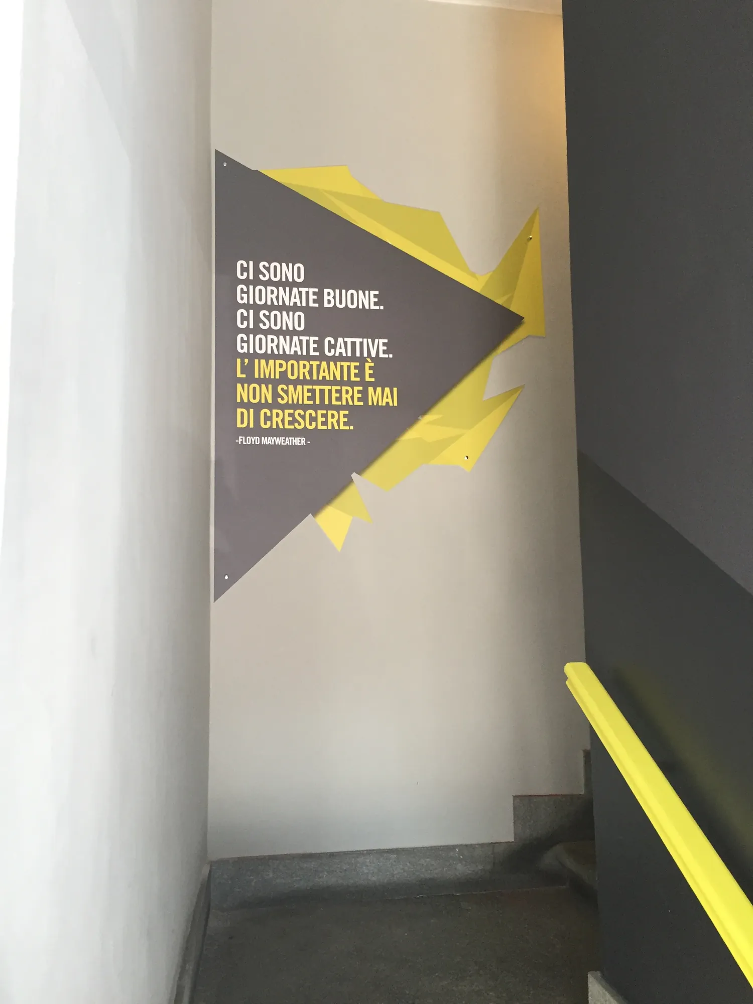 Grafica con frase motivazionale e forme gialle sulla parete della scala